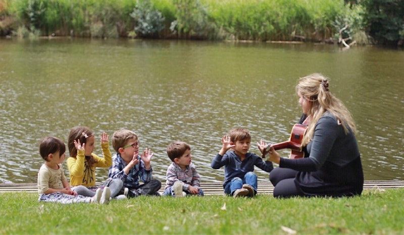 on a pond's bank a girl is playing guitar to children